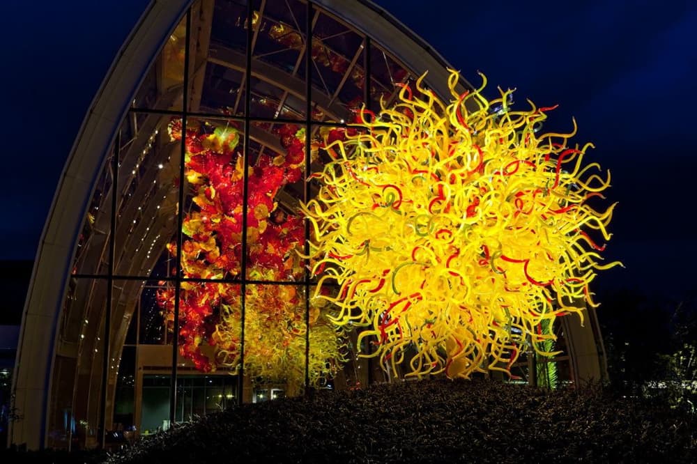 Large illuminated glass sculpture glowing at night outside a glass-and-steel gallery, with feature lighting powered by H&M Electric
